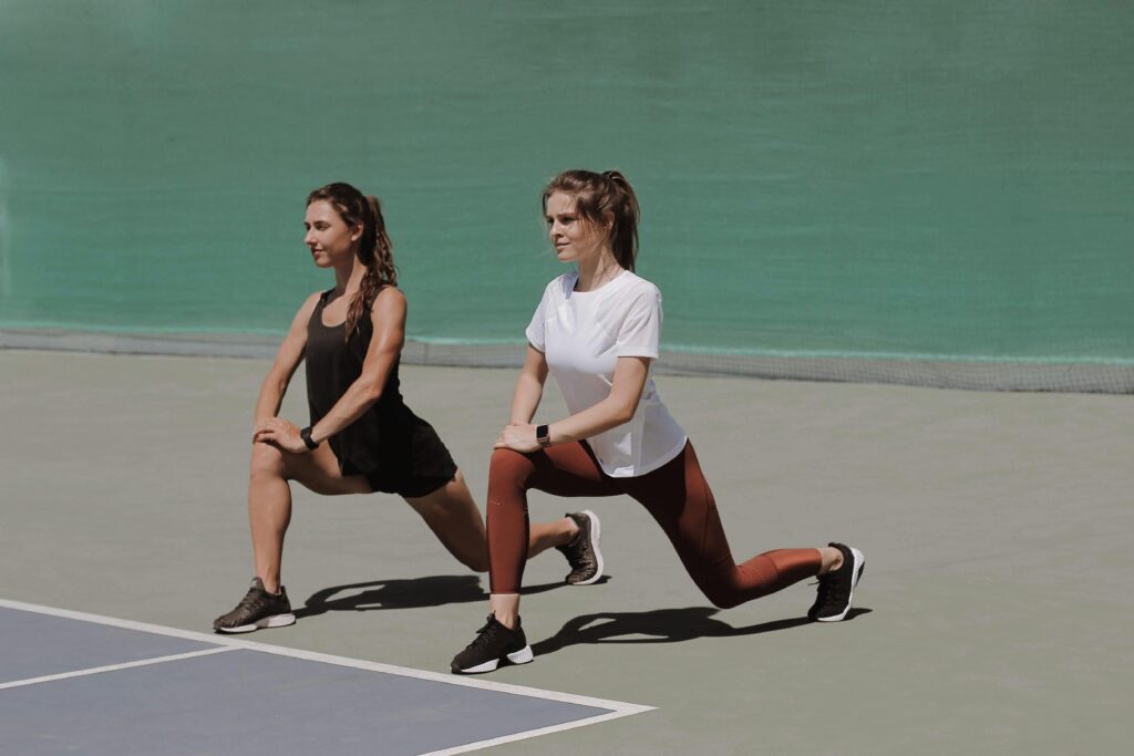 Two women perform lunges on an outdoor court, showcasing fitness and healthy lifestyle.